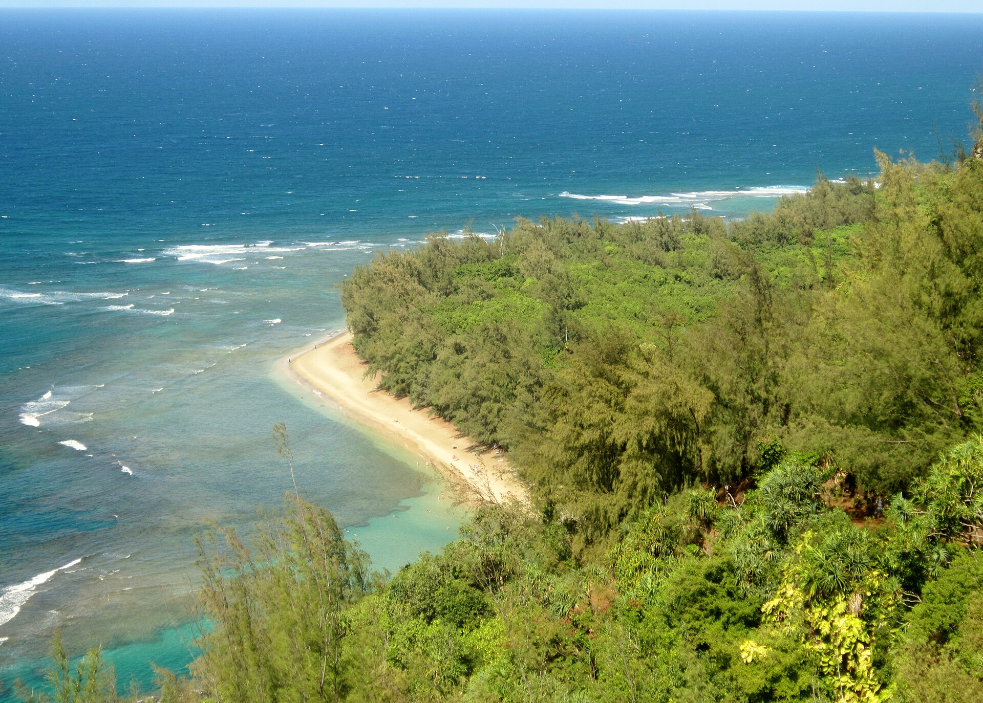 The Nāpali coast seen from high on the Kalalau Trail: turquoise reef, a crescent of sand and steep green cliffs running out to sea