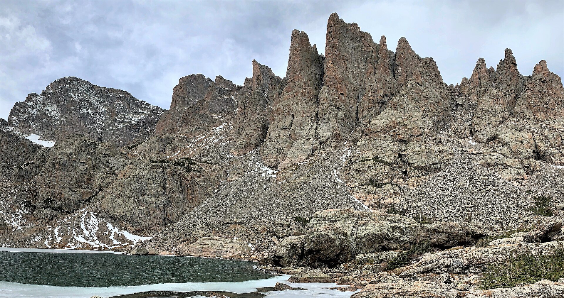 The jagged Cathedral Spires rising directly above Sky Pond, with ice still covering part of the water and snow in the gullies
